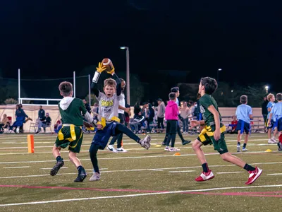 Youth player in white jersey catching a football mid-air while surrounded by defenders at night