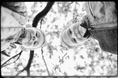 Black and white low-angle shot of two boys peering down at the camera through tree branches