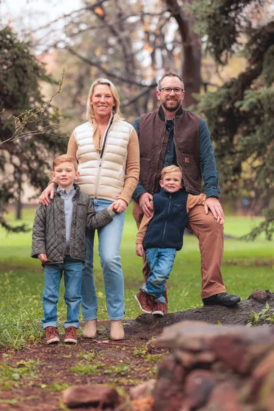 Family of four standing together in a lush green park with autumn trees in the background