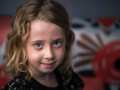Young girl with curly blonde hair, blue eyes, and freckles giving a gentle knowing smile