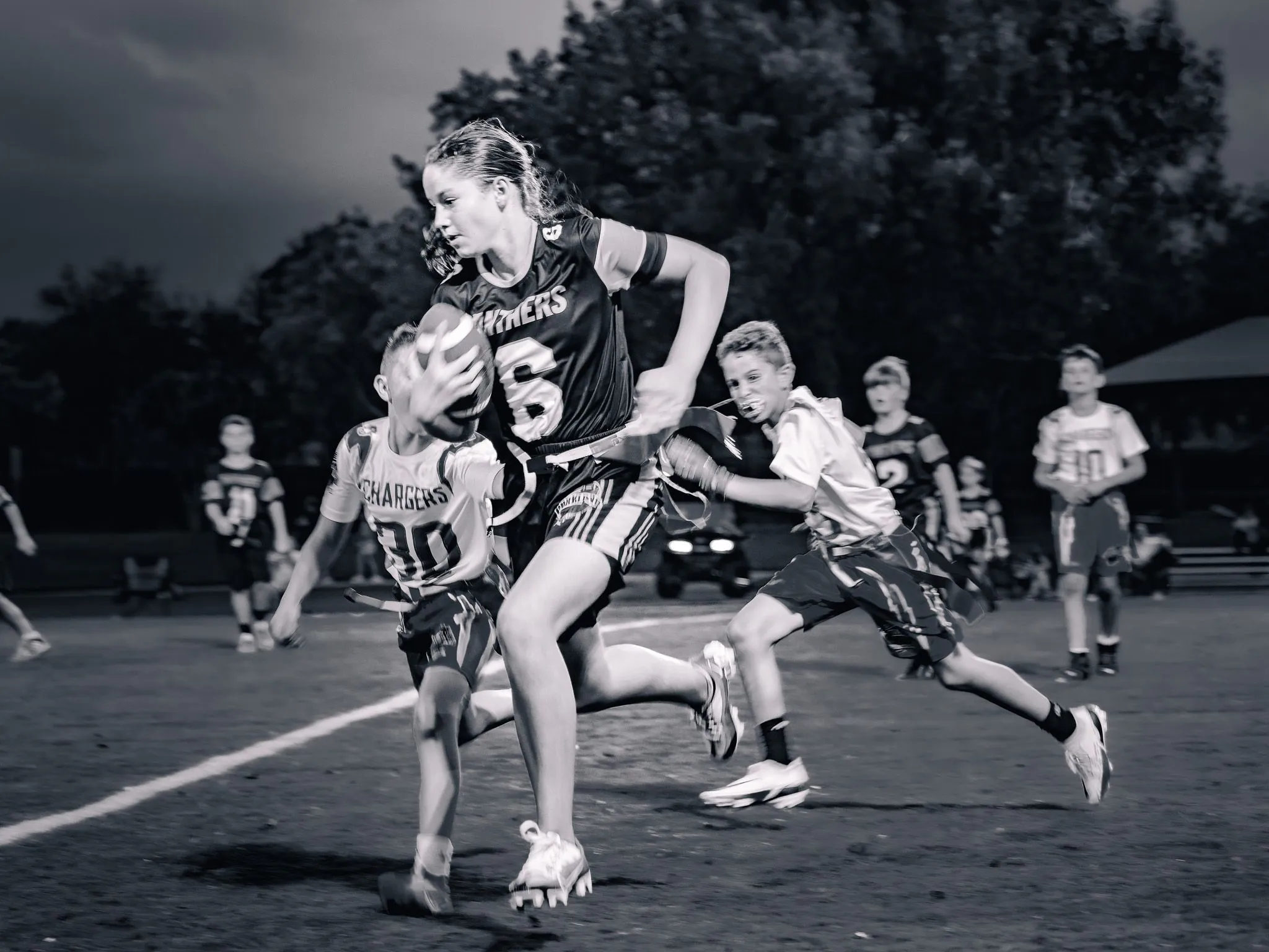 Black and white action shot of a girl running with the football while defenders chase her