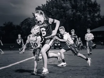 Black and white action shot of a girl running with the football while defenders chase her