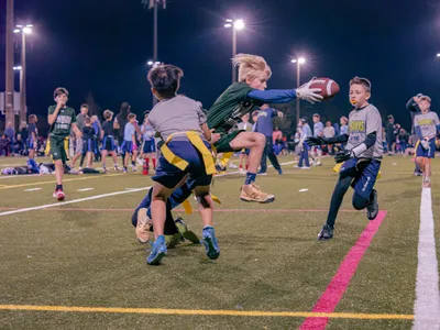 Boy in green jersey dodging defenders while running with the football during a night game