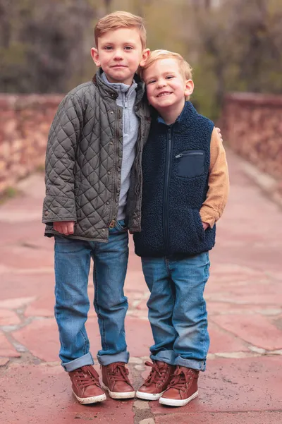Two young brothers standing together on a red stone path in fall jackets and jeans
