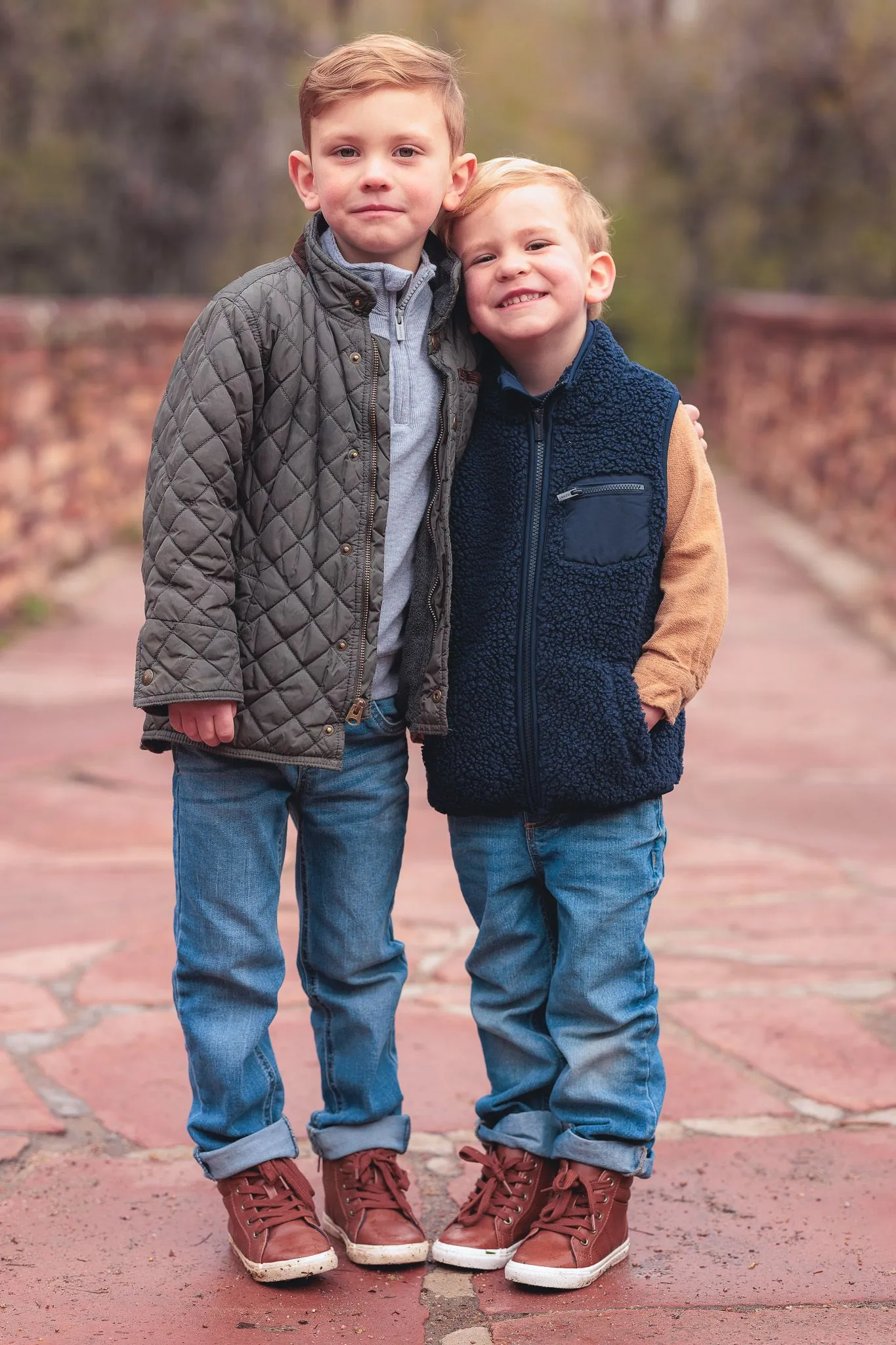 Two young brothers standing together on a red stone path in fall jackets and jeans