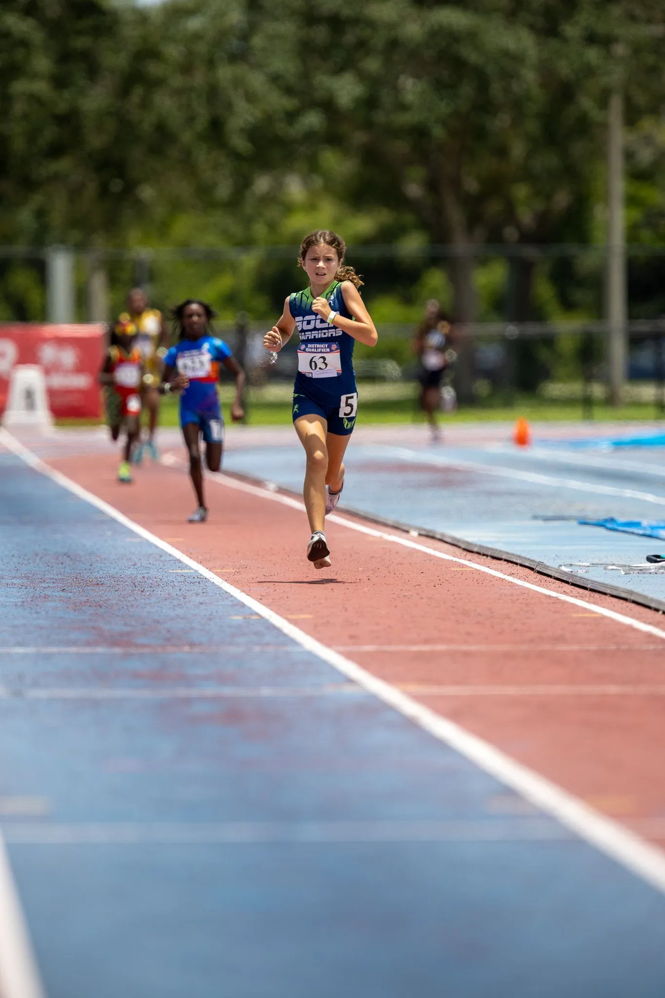 Young girl in Boca Warriors uniform leading a pack of runners down the track homestretch