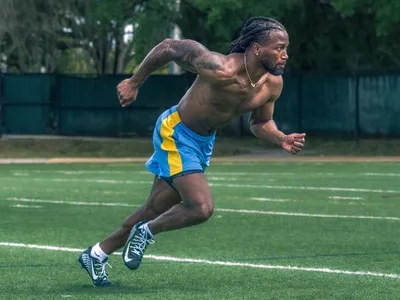 Athlete in blue shorts exploding off the line in a powerful sprint on a green turf field