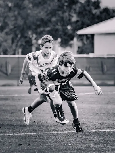 Black and white action shot of a youth football player cutting with the ball past a defender