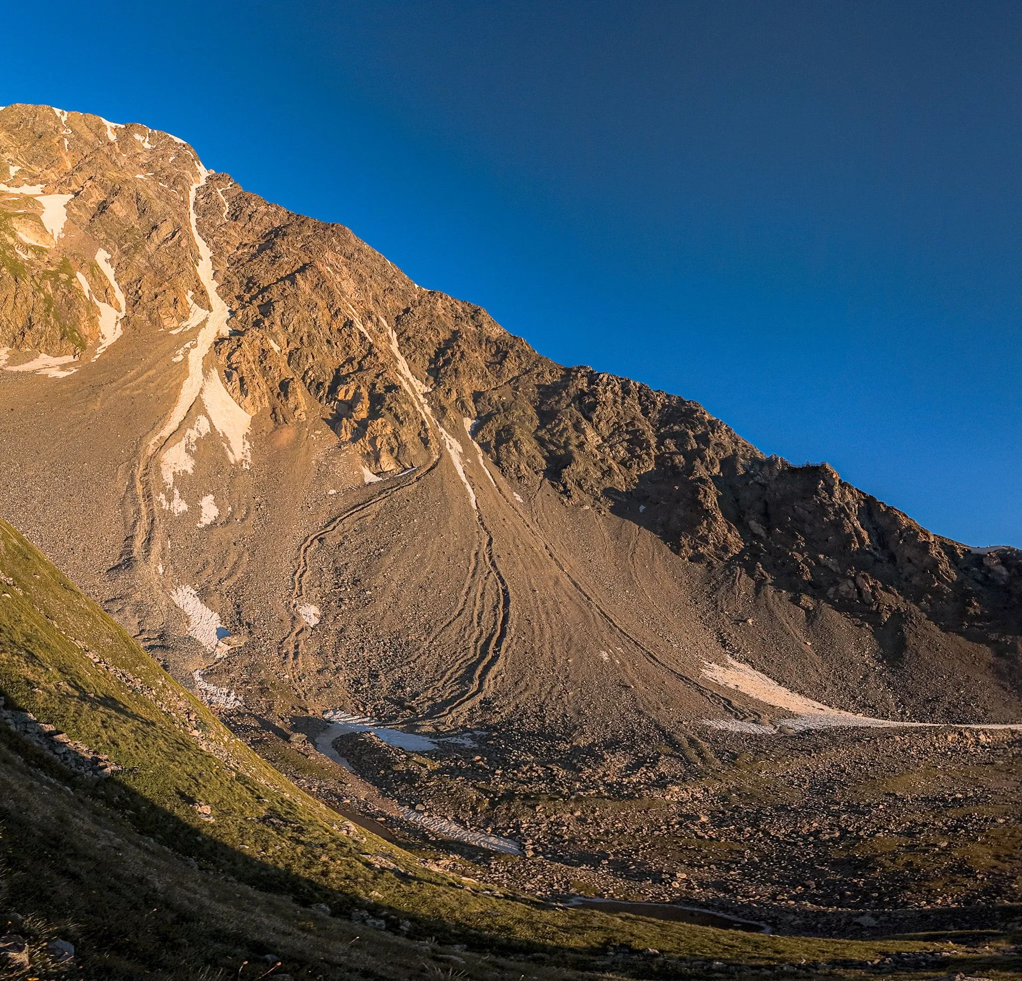 Aerial drone view of a massive mountain face with winding switchback trails at golden hour
