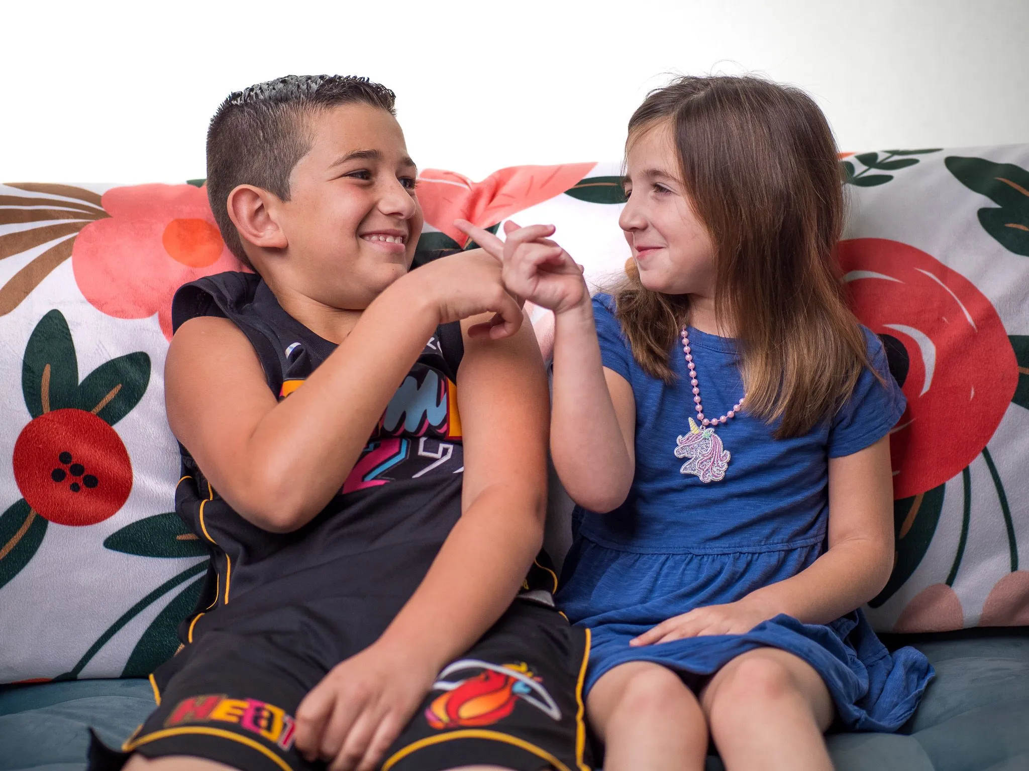 Brother and sister sitting on a couch smiling at each other with a playful finger gesture