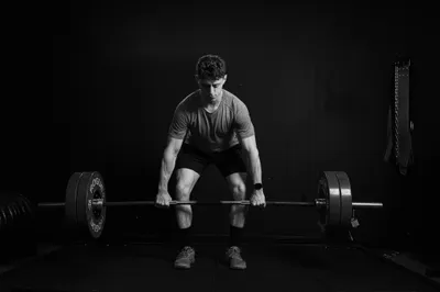 Black and white photo of a focused man gripping a loaded barbell at the start of a deadlift