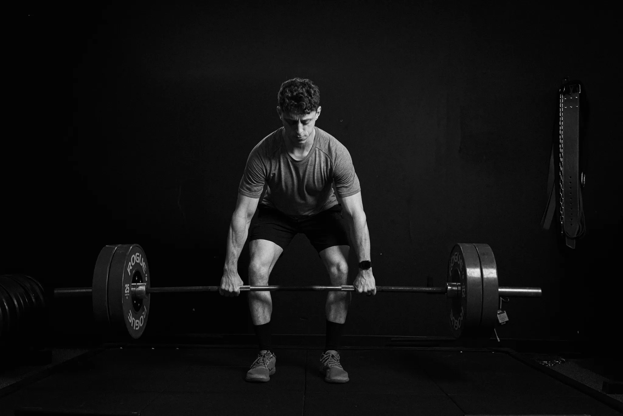 Black and white photo of a focused man gripping a loaded barbell at the start of a deadlift