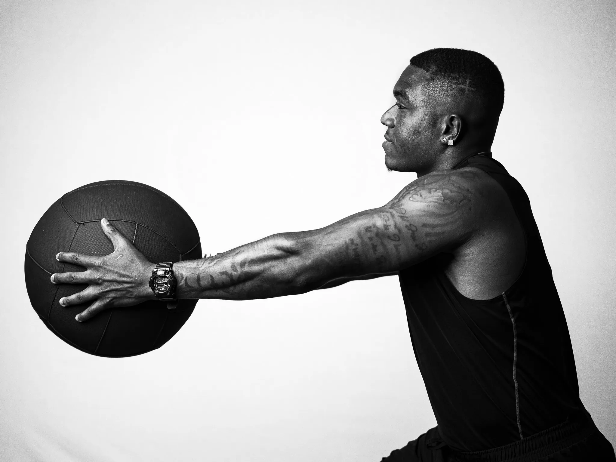 Black and white profile of tattooed male athlete extending a medicine ball with both arms in studio