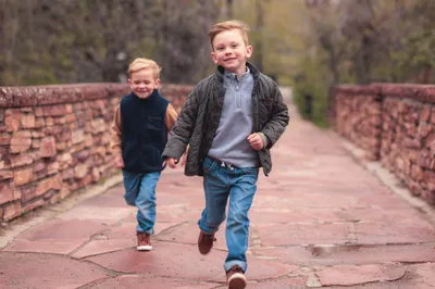 Two young brothers running and laughing across a red stone bridge on a fall afternoon