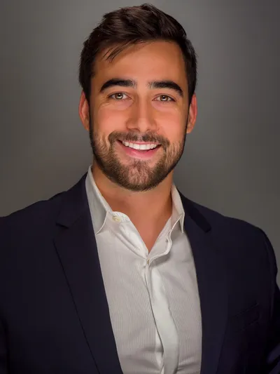 Young man with a beard in a navy blazer and white shirt smiling for a professional headshot