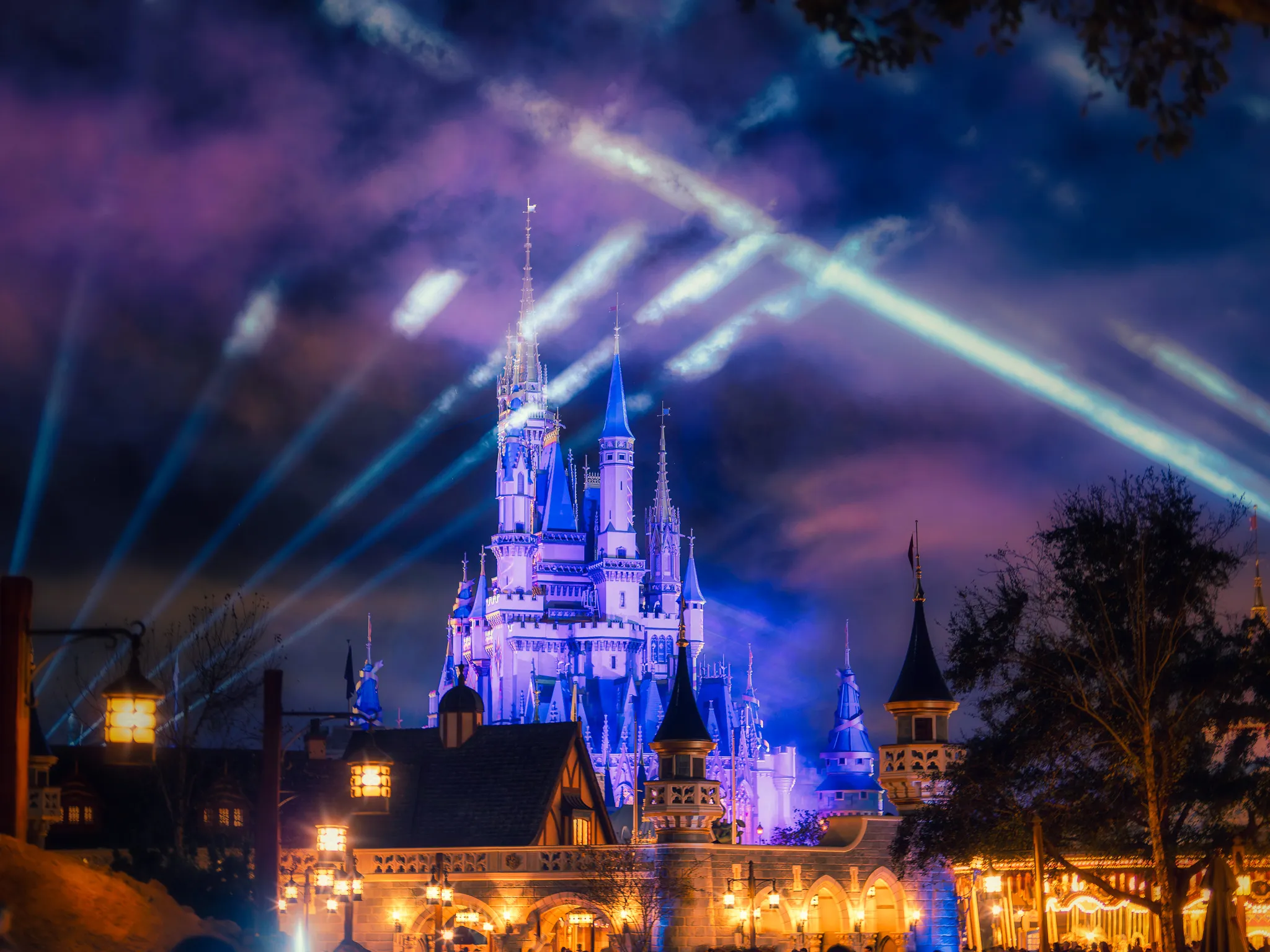 Cinderella Castle at Walt Disney World illuminated in blue with spotlights streaming across a dramatic purple night sky