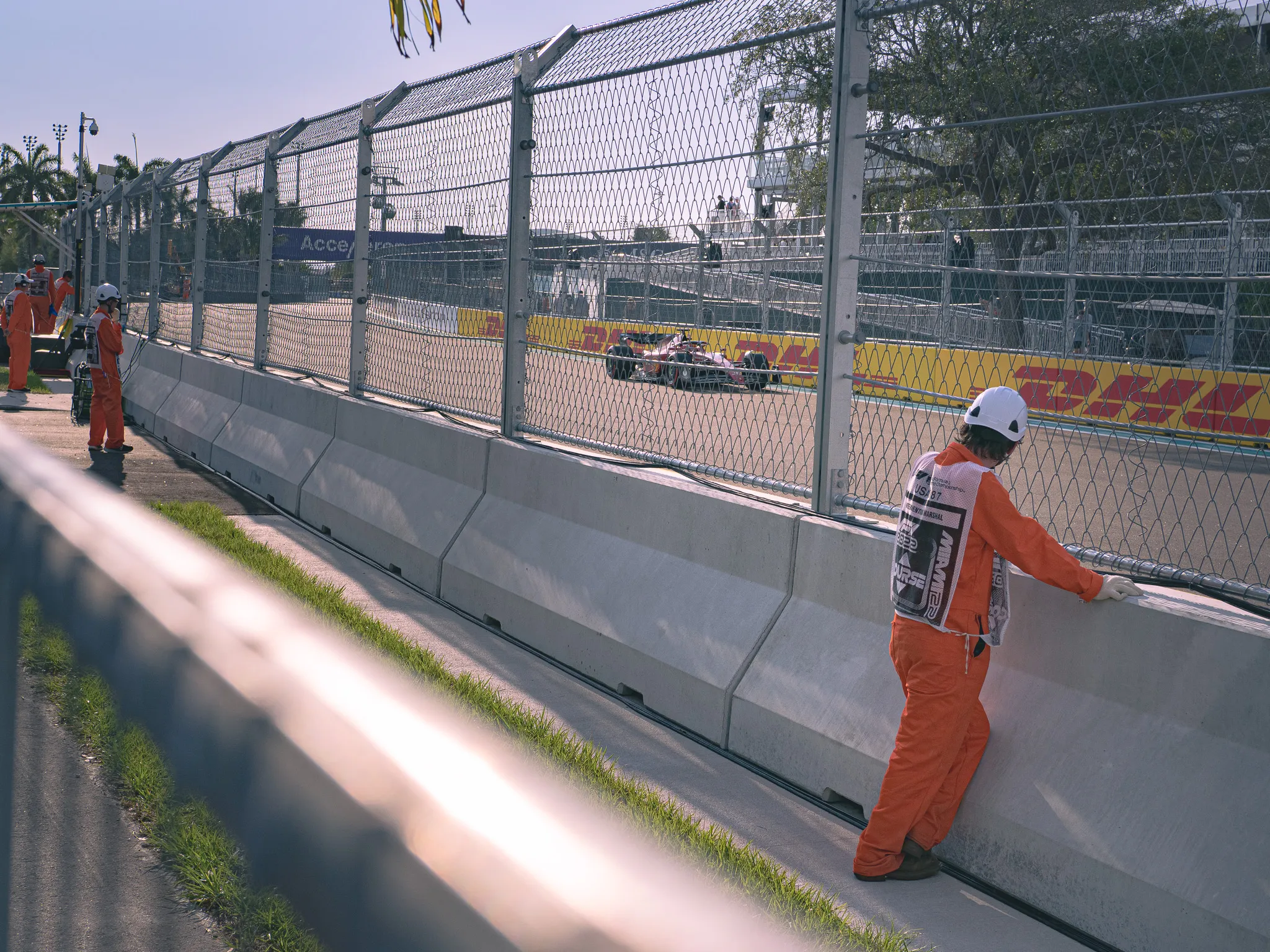 Formula One race track with two marshals in orange jumpsuits standing trackside behind concrete barriers and safety fencing