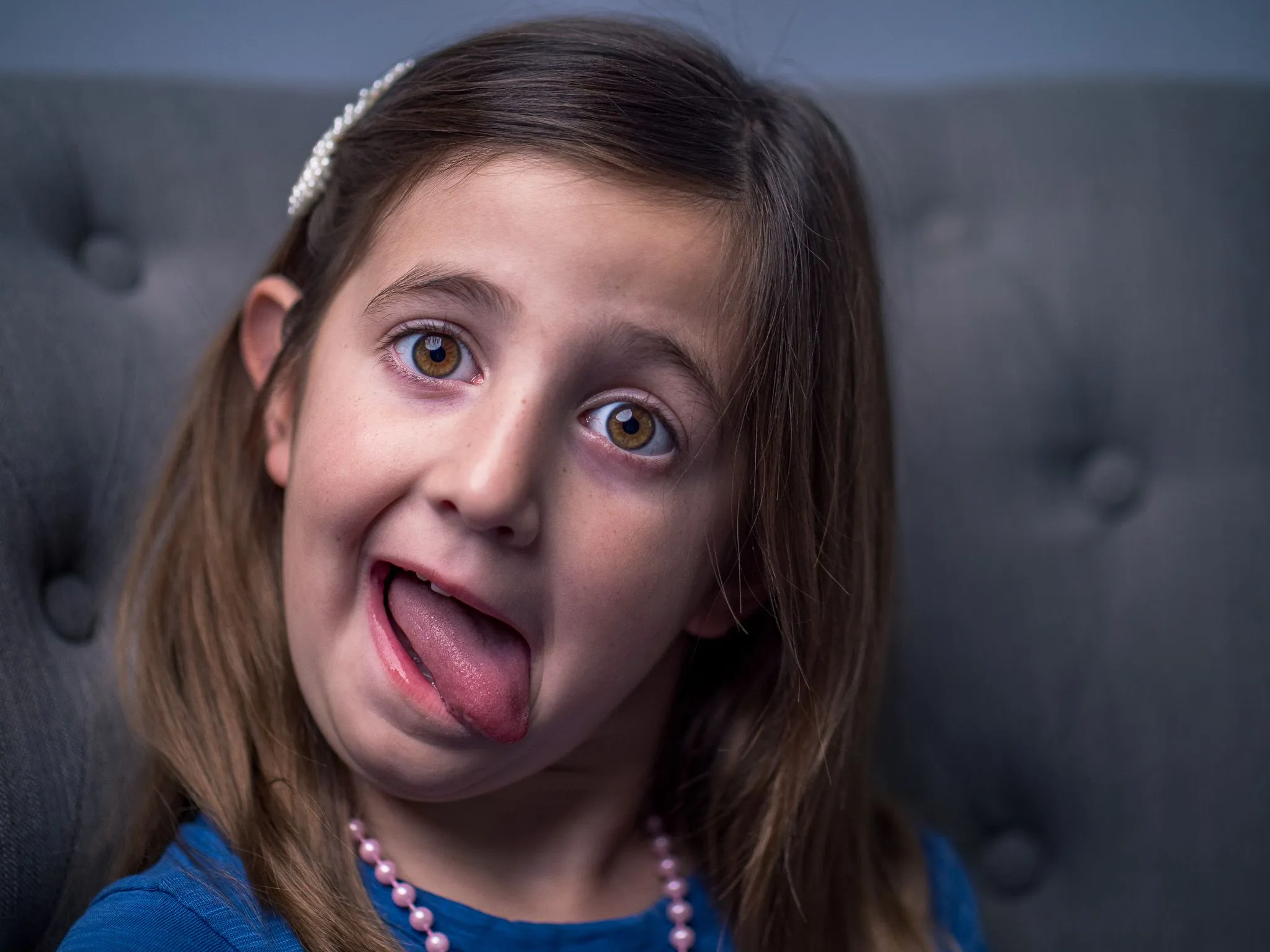 Young girl with brown hair sticking her tongue out playfully against a tufted gray backdrop