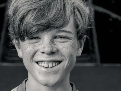 Black and white close-up of a freckled boy with a wide, joyful smile and tousled hair