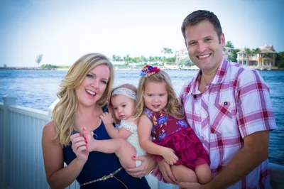 Smiling family of four with two young daughters posing on a waterfront dock at golden hour