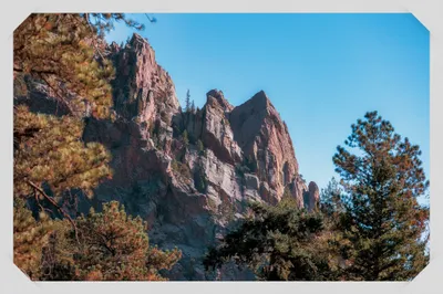 Red sandstone rock formations rising above pine trees against a clear blue sky in Colorado foothills