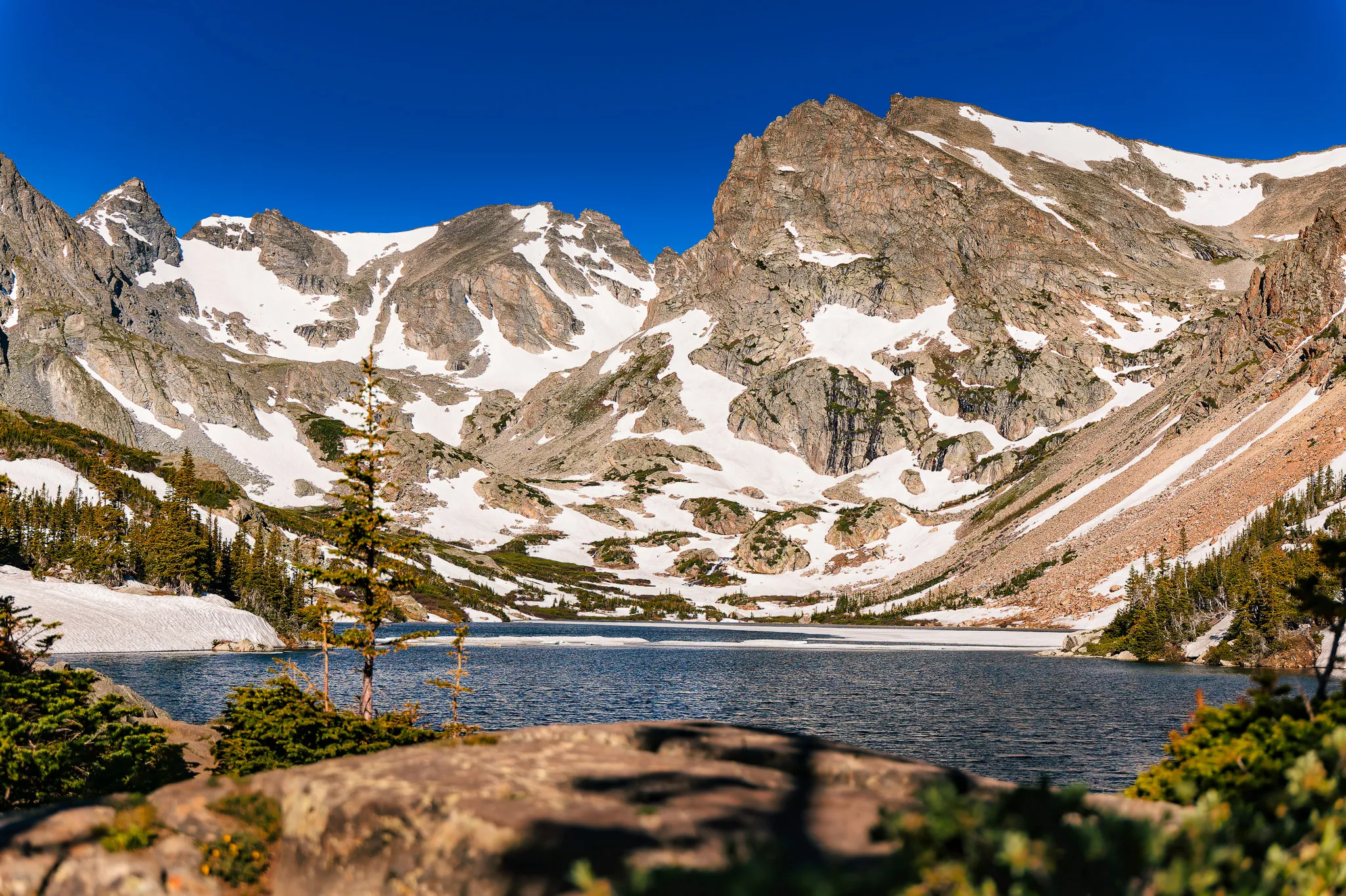 Alpine lake surrounded by snow-covered rocky mountain peaks under a clear blue sky in Colorado