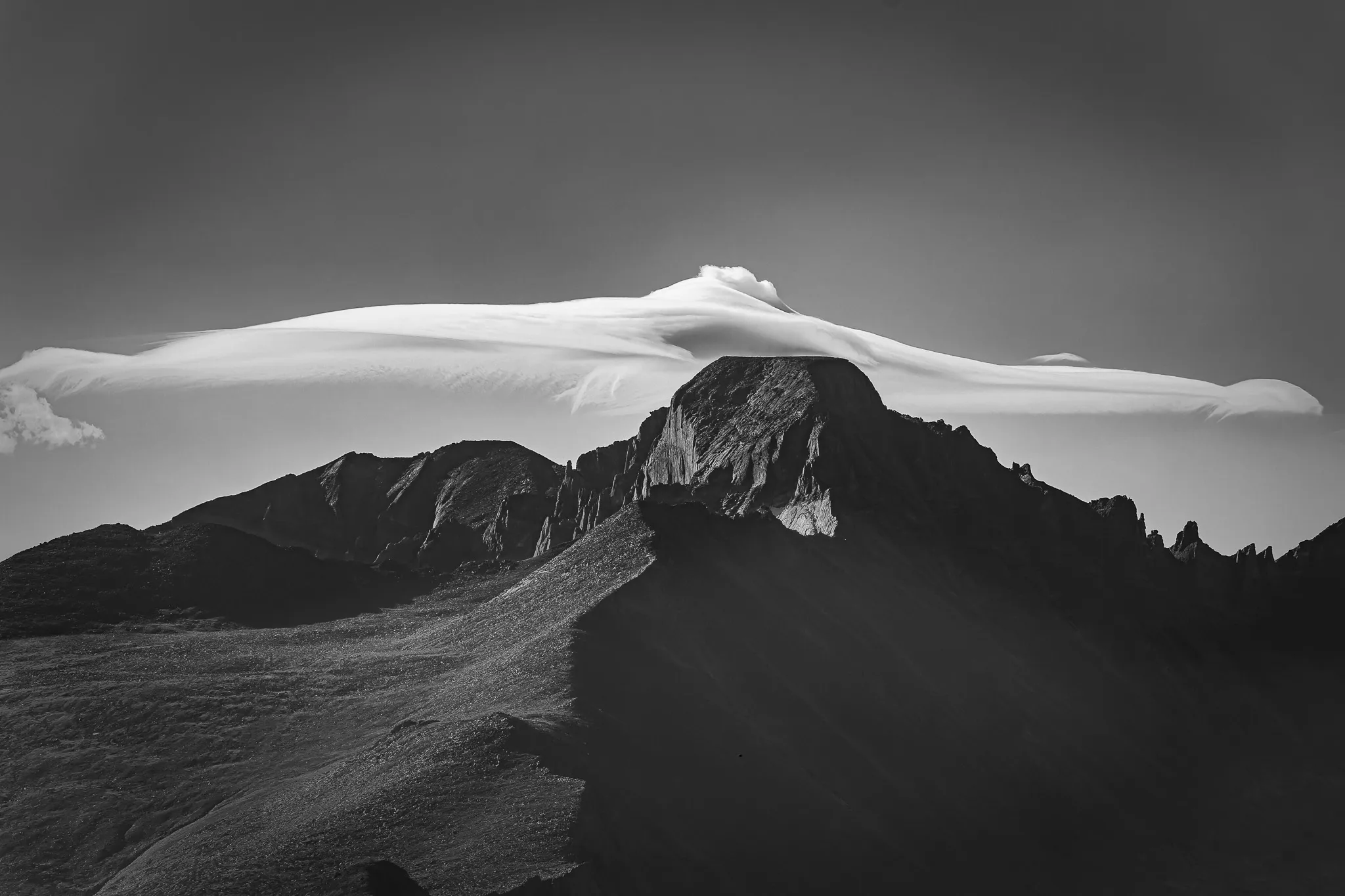 Dramatic lenticular cloud draped over a mountain peak in black and white with rugged ridgelines
