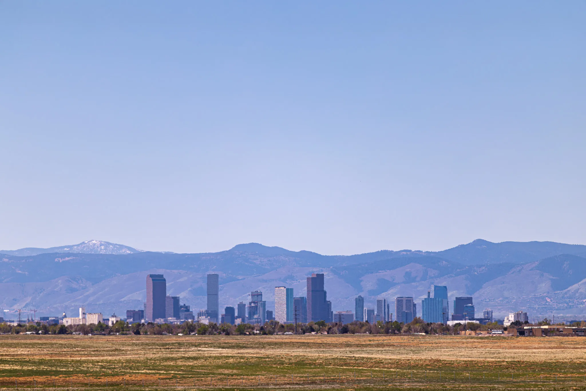 Denver skyline viewed from open plains with the Rocky Mountain foothills and clear blue sky behind the city