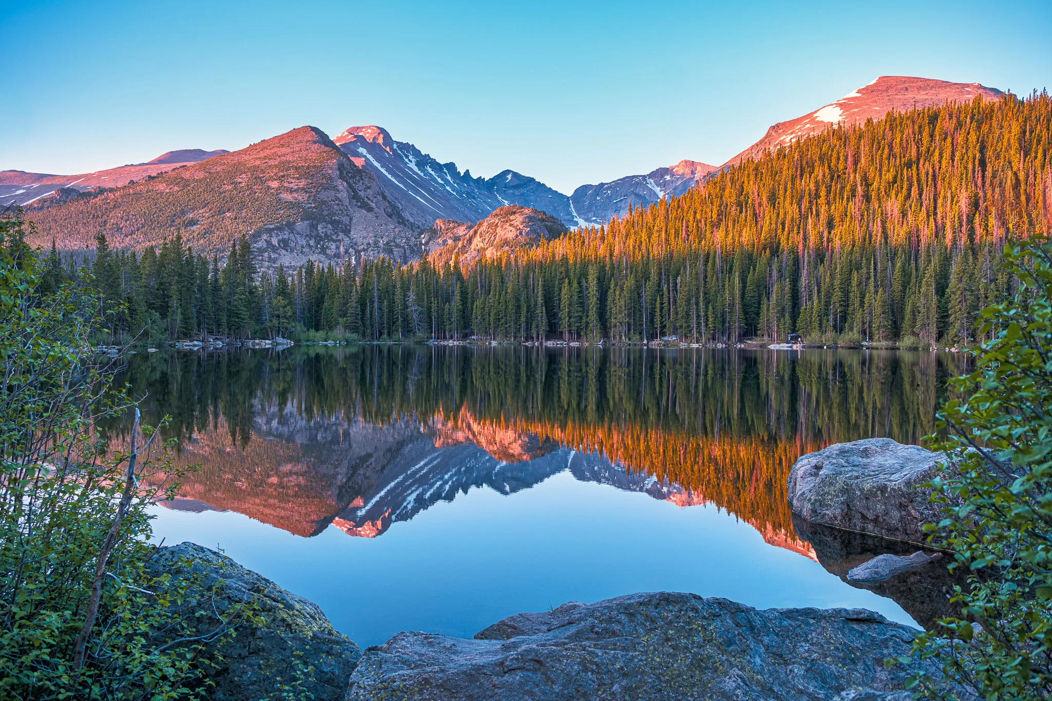 Bear Lake in Rocky Mountain National Park at sunrise with mirror-still water reflecting snow-capped peaks and pine forest
