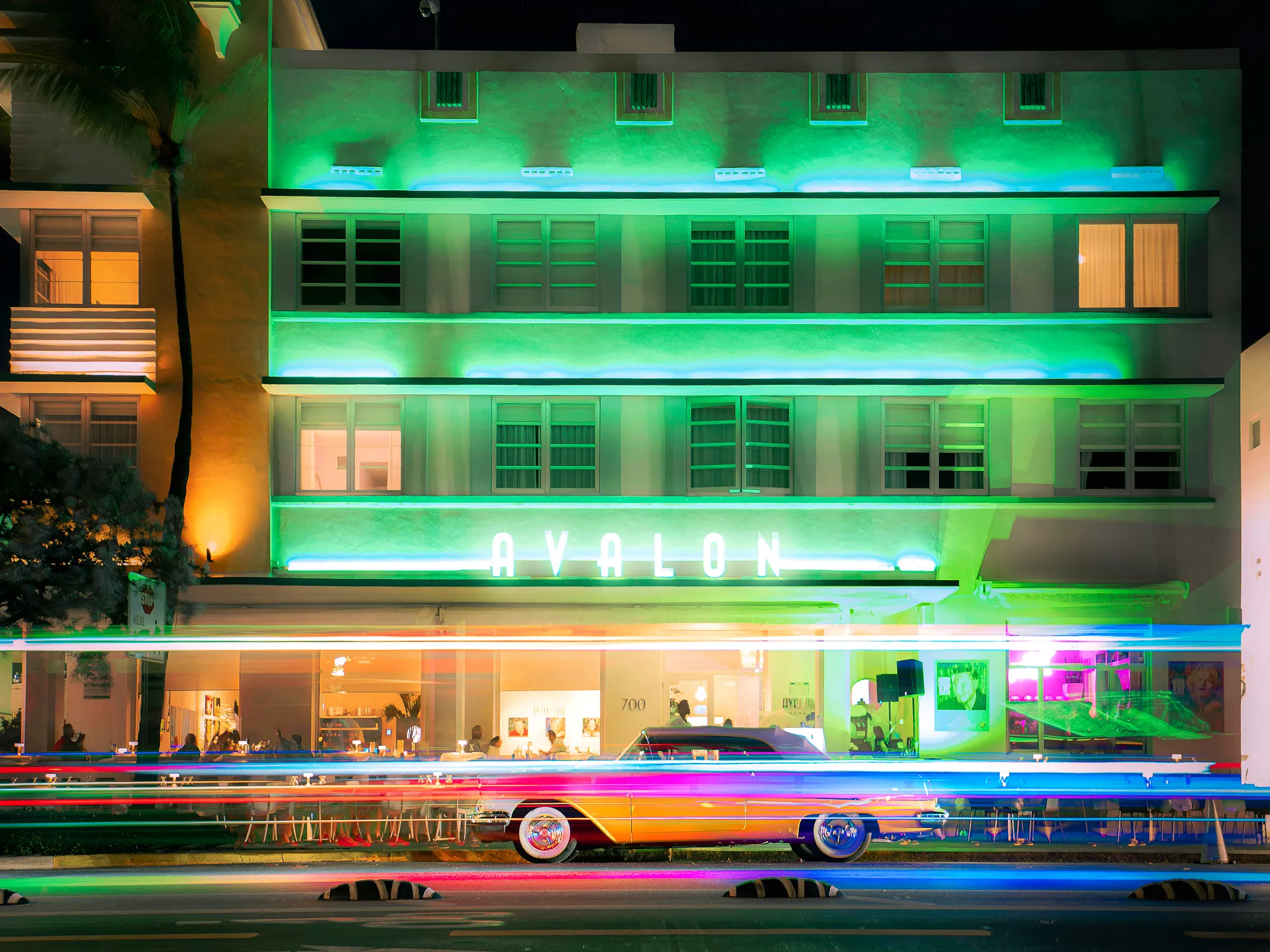 Avalon Hotel on Miami Beach at night lit in green neon with a classic car parked out front and light trails on the street