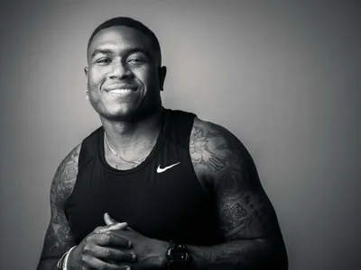 Young athletic man with tattoo sleeves smiling warmly in black Nike tank top, studio black and white portrait