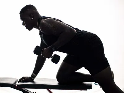 Silhouetted athlete performing single-arm dumbbell row on a bench, backlit studio fitness portrait
