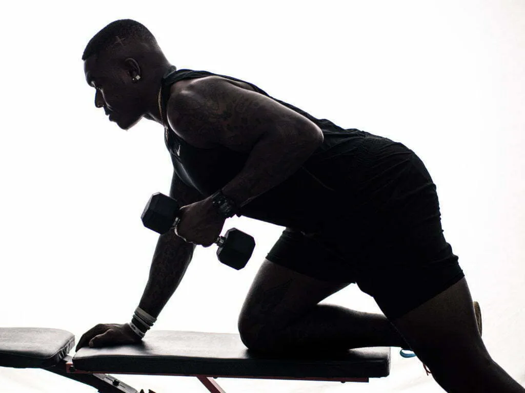 Silhouetted athlete performing single-arm dumbbell row on a bench, backlit studio fitness portrait