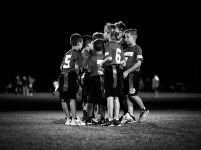 Youth flag football team huddled together with their coach on the field at night, black and white photo