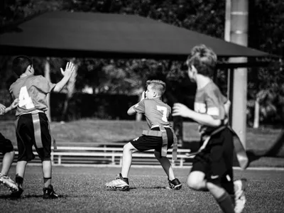 Three boys playing youth flag football, center player throwing the ball on a daytime field, black and white photo