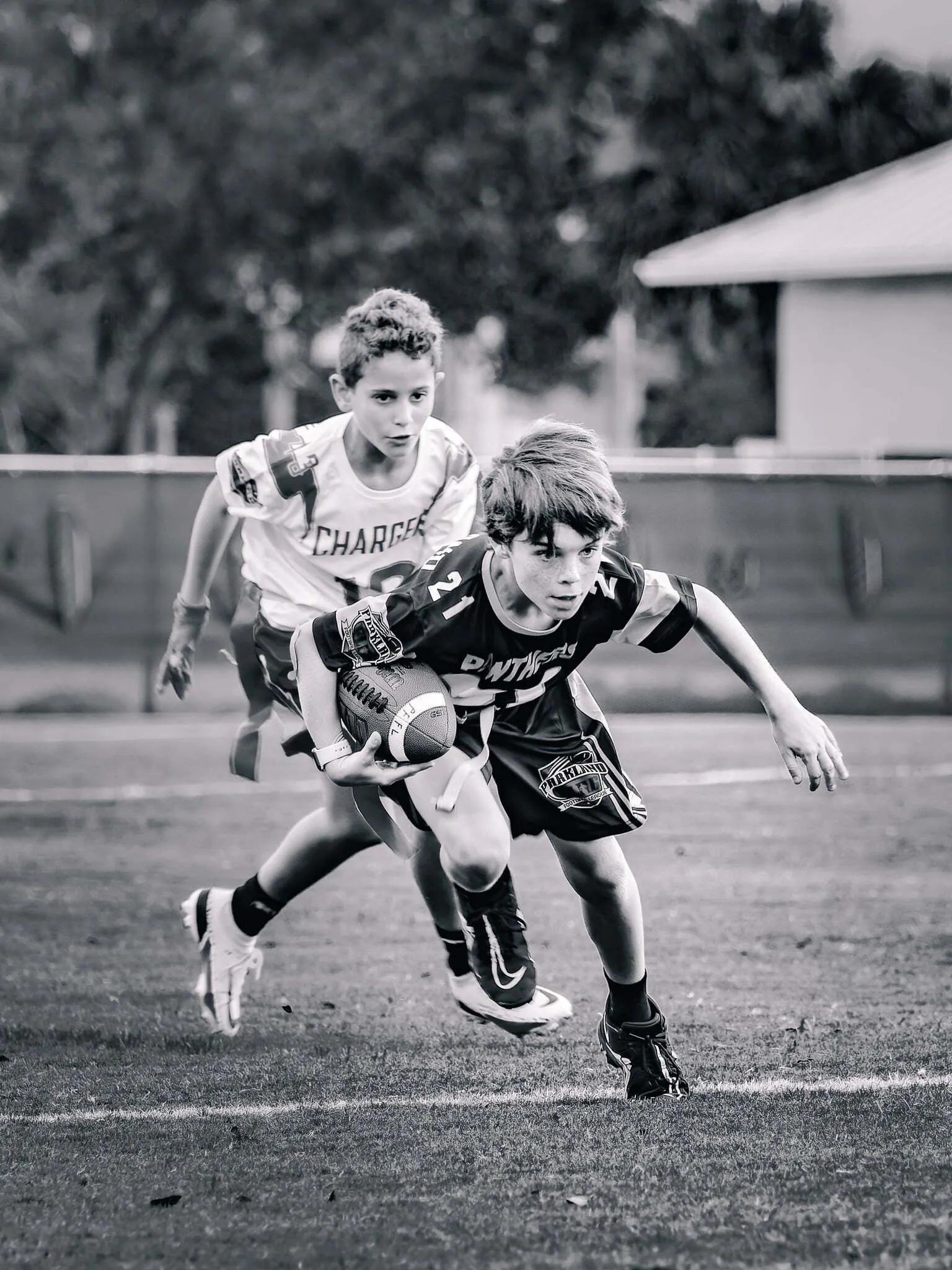Black and white action shot of two boys playing flag football, one Panthers player cutting sharply while carrying the ball past a Chargers defender