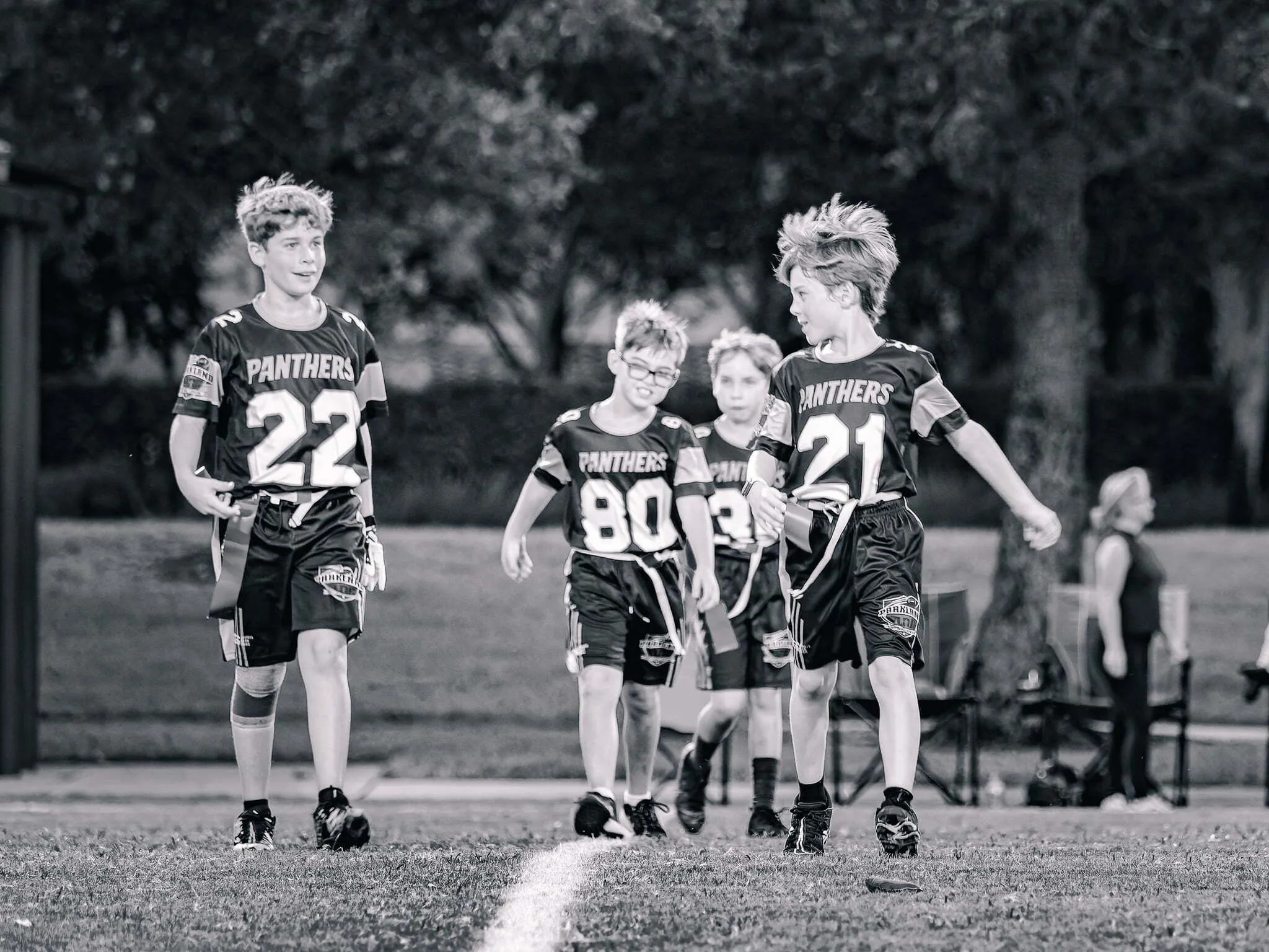 Black and white photo of four Panthers teammates walking and smiling together on the field after a youth flag football game