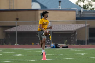 Teen athlete in yellow school shirt doing high knee warm-up drill on turf football field with mouthguard