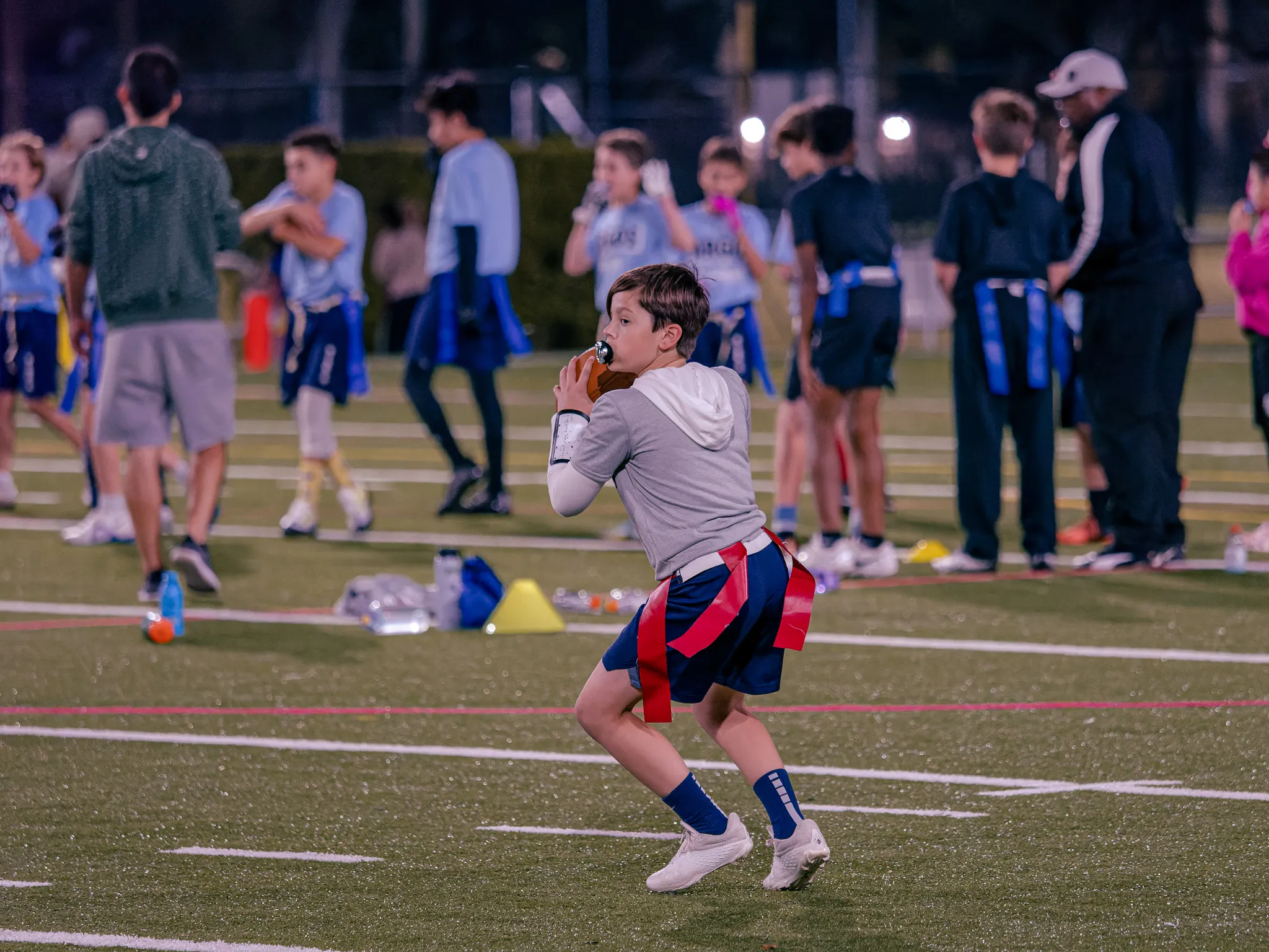 Young boy eating a snack on a football field at night with teammates and spectators in the background